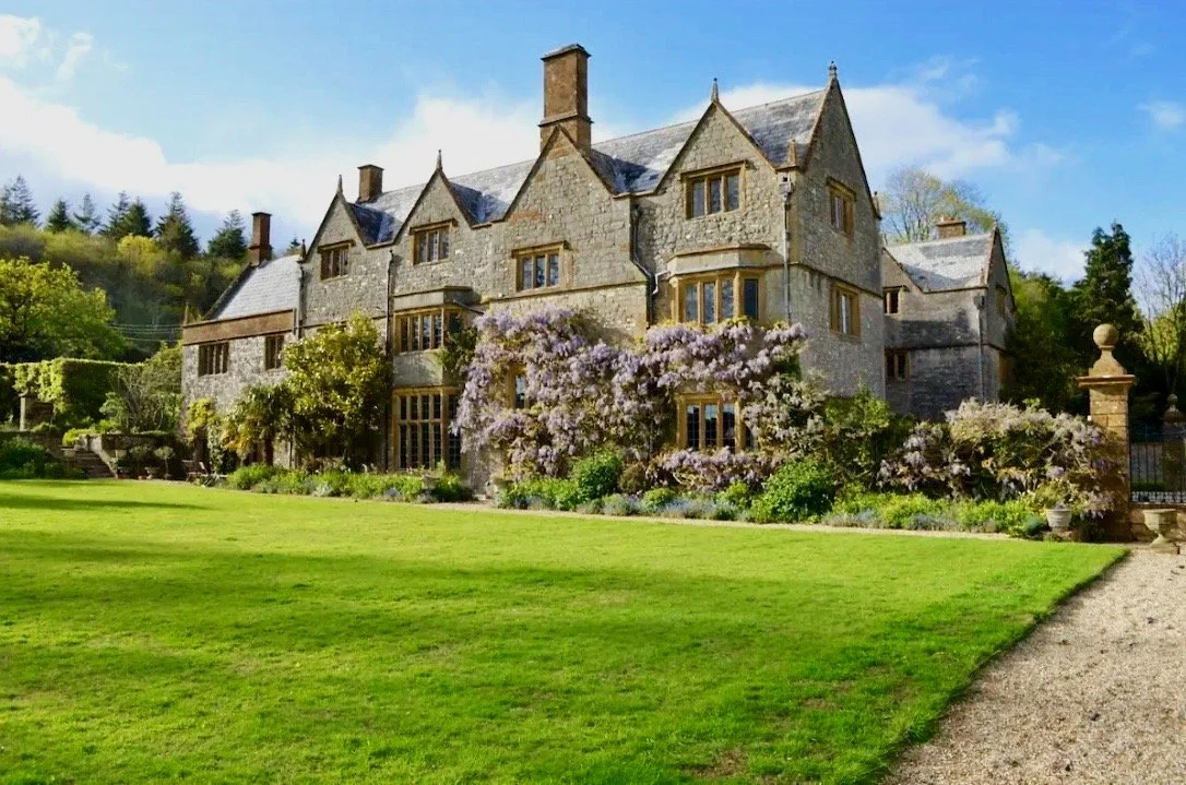 The long golden stone facade of the manor seen across the lawns
