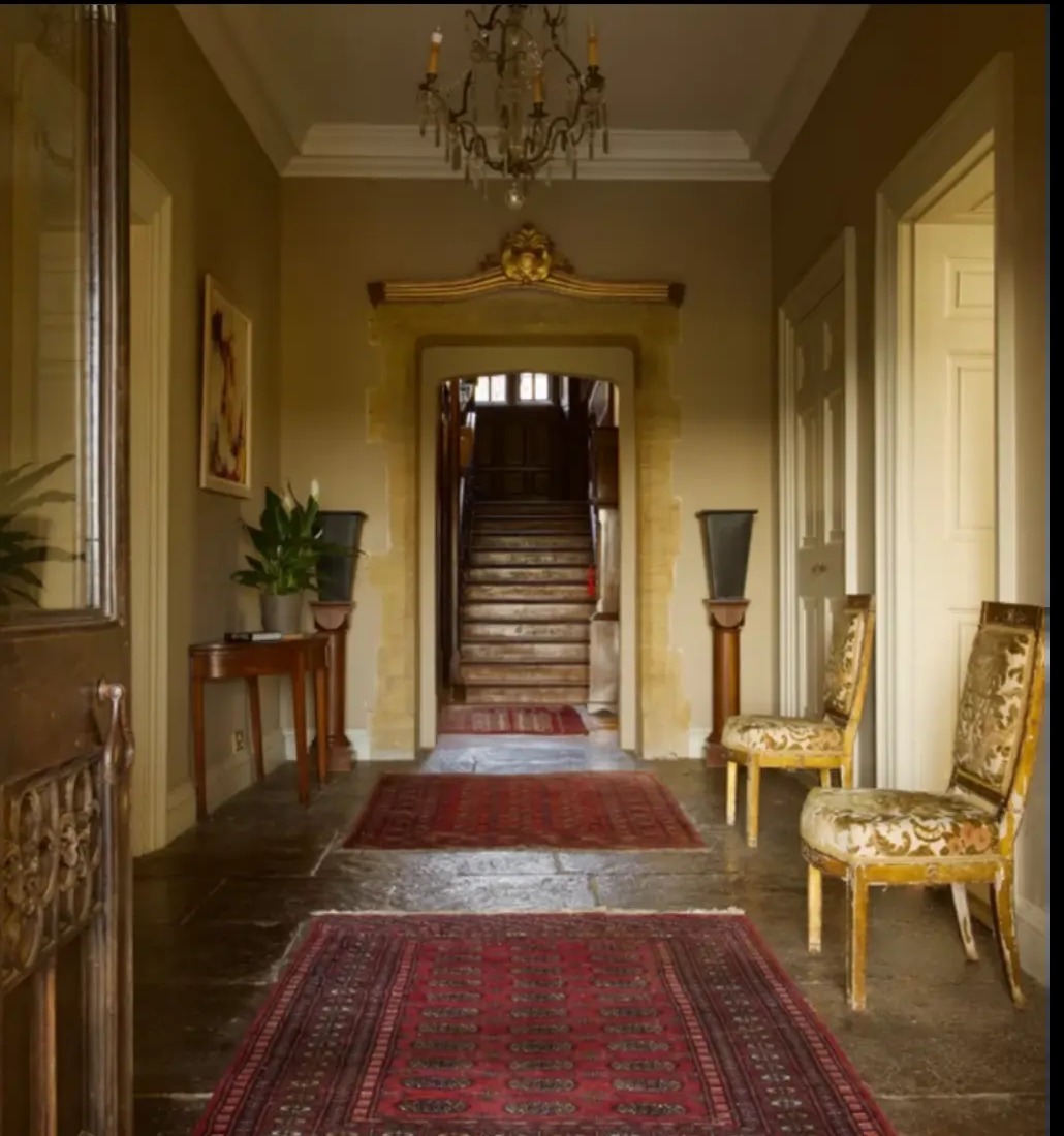 A grand interior hallway with red rugs, panelling and a chandelier